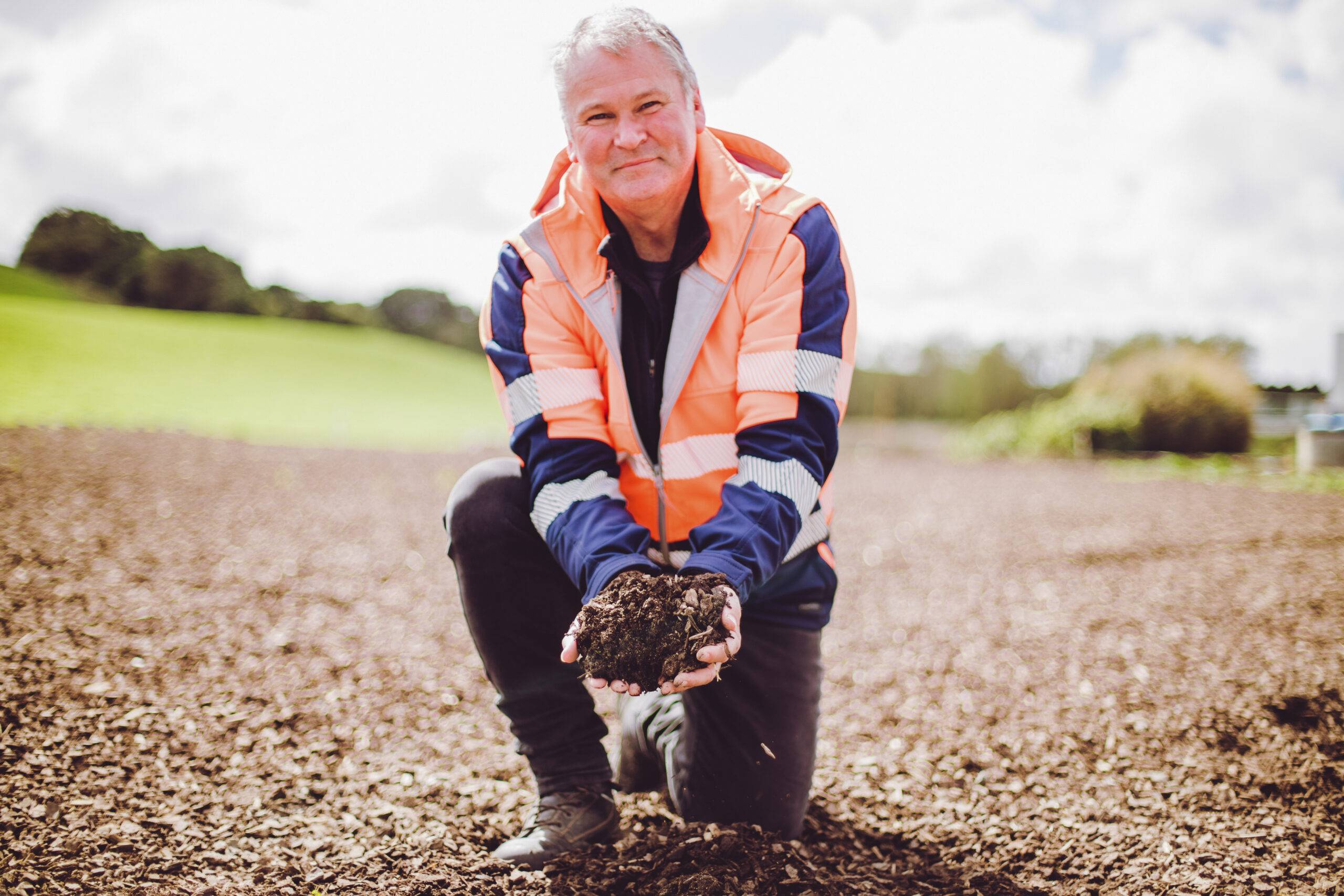 Environmental Manager crouching on a biofiltration bed and holding bio-filter media