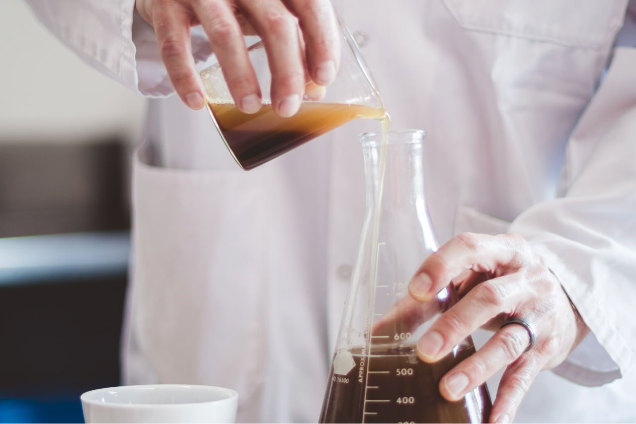 Person in white lab coat pouring liquid in measuring beaker